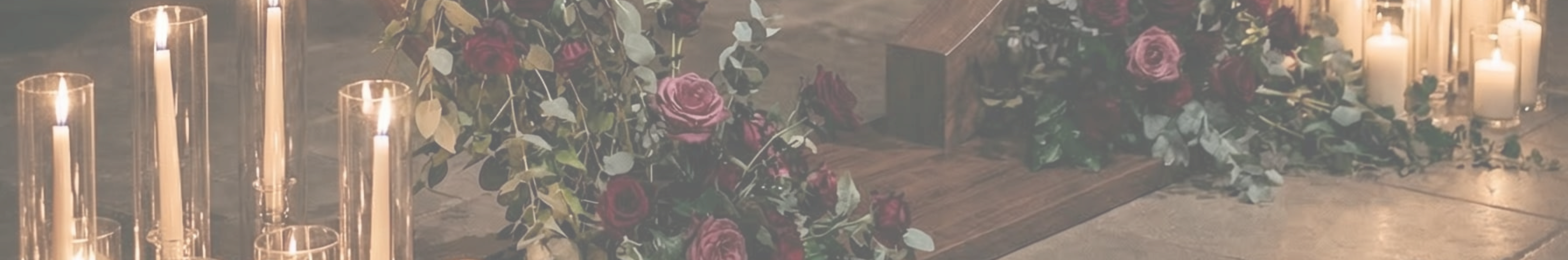 Dark red and burgundy florals with eucalyptus draped beside the arch's wooden base, lit by rows of candlelight